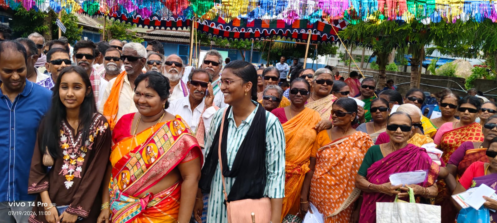 Crowd of people wearing sunglasses and holding packets at a community eye camp