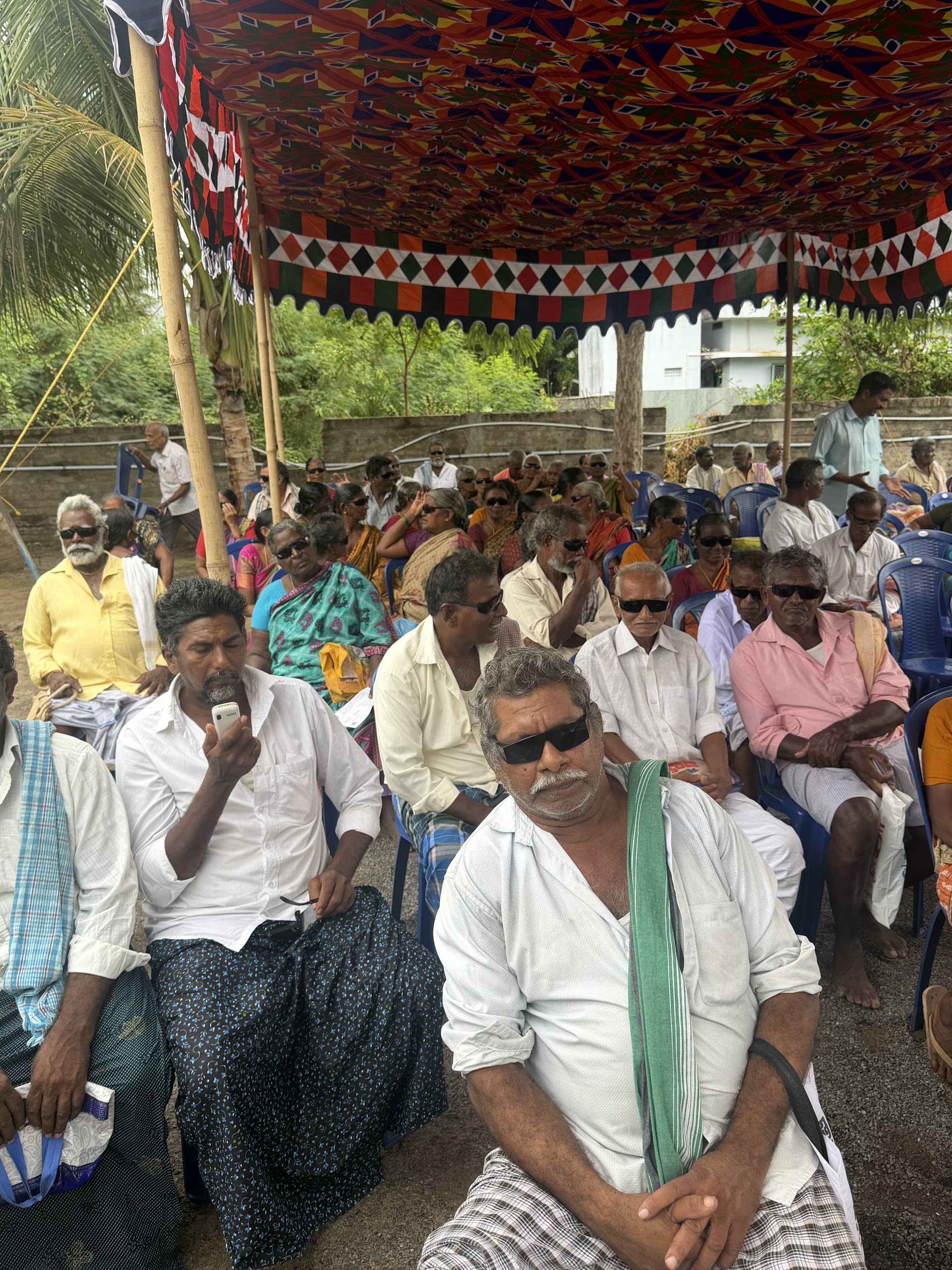 Community members seated under a colorful canopy at a health camp