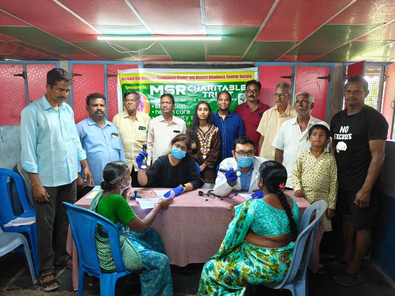 Doctors examining patients' eyes at a table during a Sankara Eye Hospital screening camp